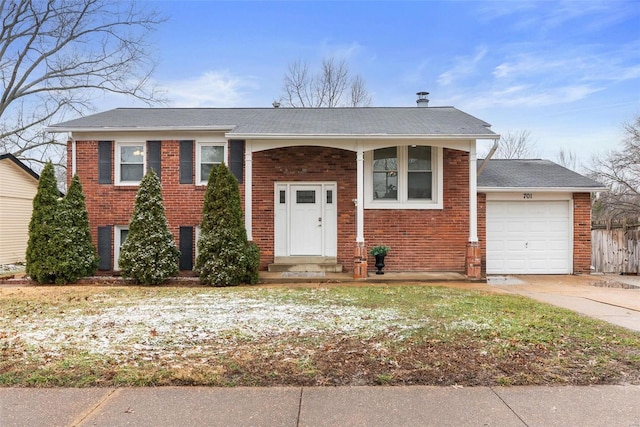 split foyer home featuring a garage, brick siding, fence, and driveway