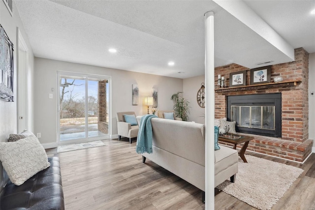 living room featuring a textured ceiling, a brick fireplace, wood finished floors, and baseboards