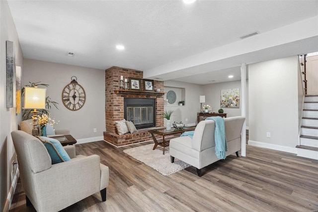 living room with baseboards, visible vents, wood finished floors, stairs, and a brick fireplace