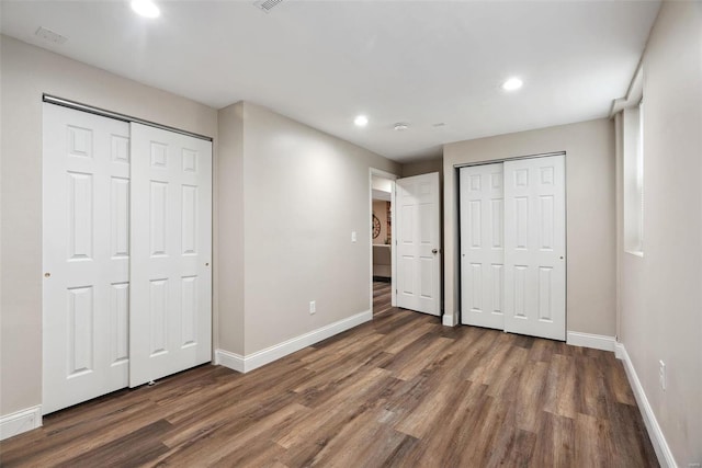 unfurnished bedroom with recessed lighting, baseboards, multiple closets, and wood finished floors