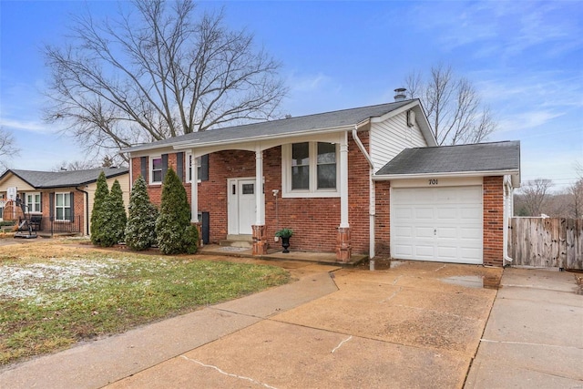 raised ranch with an attached garage, fence, concrete driveway, and brick siding