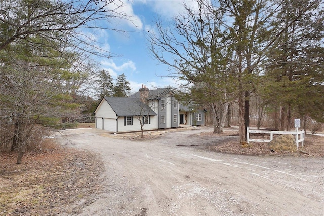 view of front facade with an attached garage, dirt driveway, and a chimney