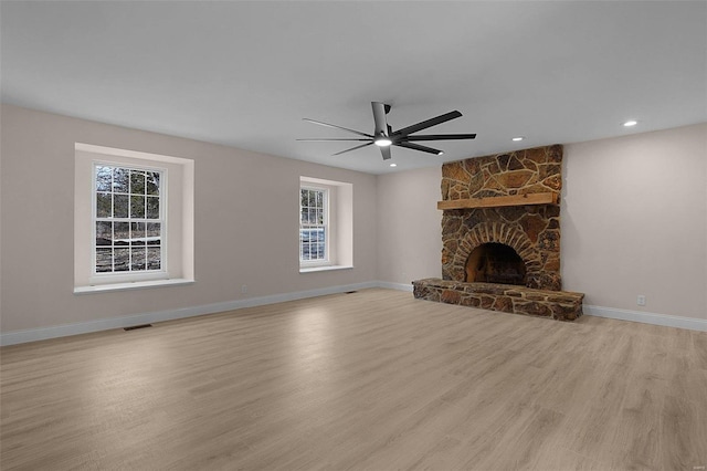 unfurnished living room with visible vents, baseboards, light wood-style flooring, ceiling fan, and a stone fireplace