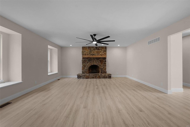 unfurnished living room with a ceiling fan, visible vents, a stone fireplace, and wood finished floors