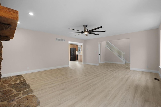 unfurnished living room featuring light wood finished floors, visible vents, baseboards, ceiling fan, and stairs