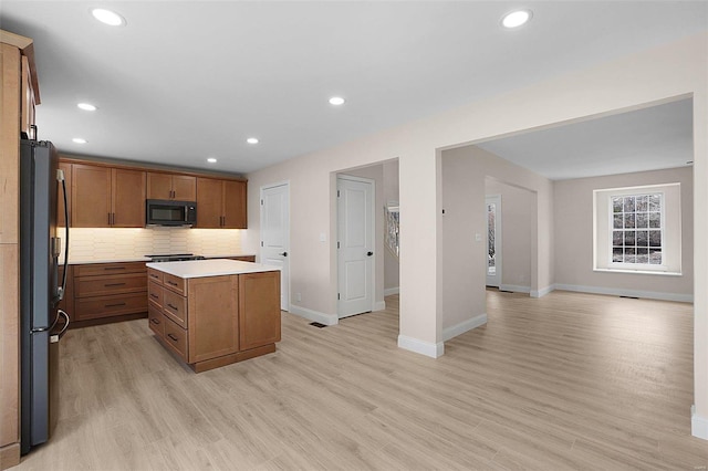 kitchen featuring tasteful backsplash, a kitchen island, light wood-type flooring, black appliances, and recessed lighting