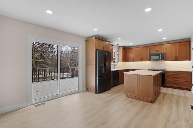 kitchen featuring decorative backsplash, light countertops, light wood-type flooring, black appliances, and a sink