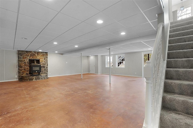 below grade area featuring stairs, a drop ceiling, a wood stove, and baseboards