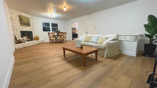 living area with baseboards, a stone fireplace, and light wood finished floors