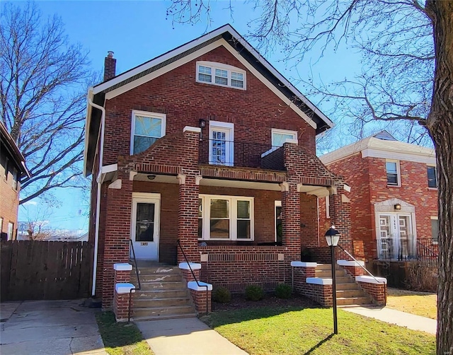 traditional home featuring covered porch, brick siding, fence, a front lawn, and a chimney