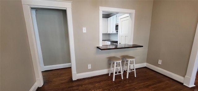 interior space featuring a breakfast bar, dark wood finished floors, dark countertops, white cabinets, and baseboards