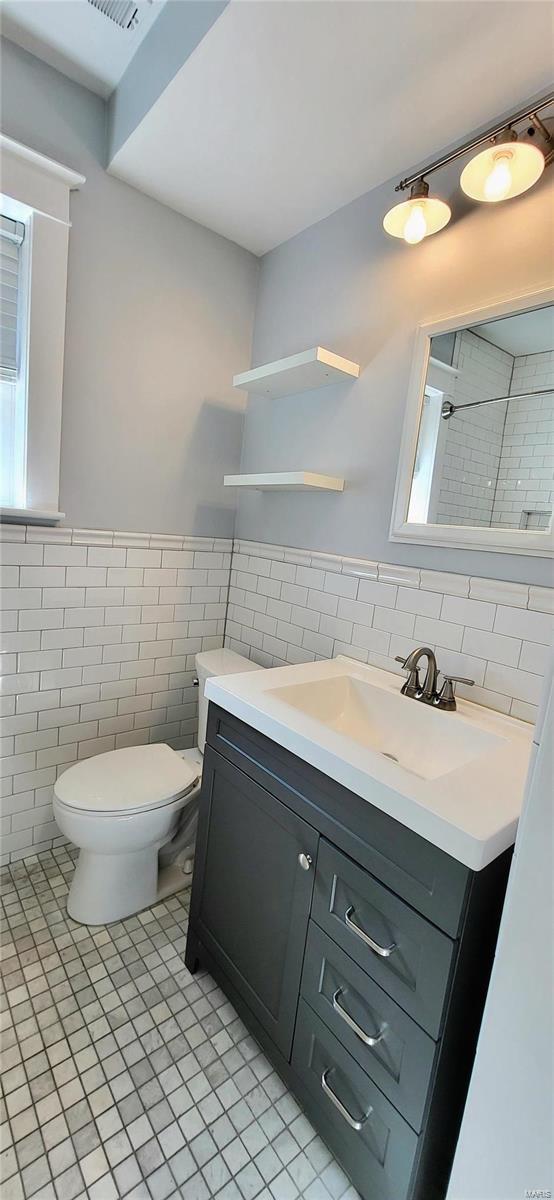 full bath featuring tile walls, toilet, wainscoting, vanity, and tile patterned flooring