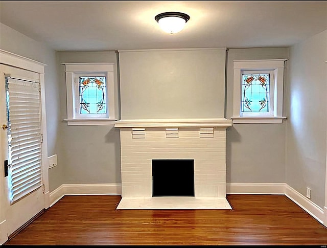 unfurnished living room with plenty of natural light, a fireplace, baseboards, and wood finished floors