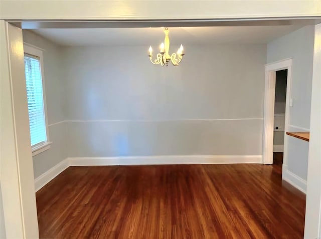 empty room with a chandelier, a wealth of natural light, baseboards, and wood finished floors