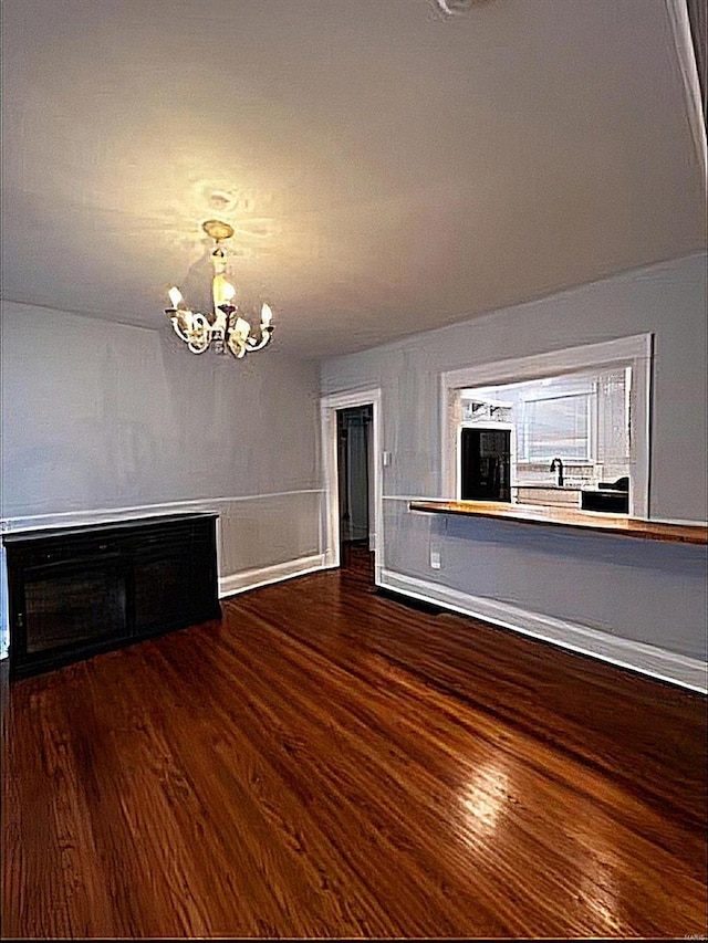 unfurnished living room with dark wood-style floors, a chandelier, and baseboards