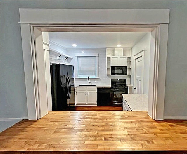 kitchen featuring black appliances, white cabinets, a sink, and light countertops