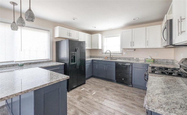 kitchen featuring pendant lighting, light wood-style floors, white cabinets, a sink, and black appliances