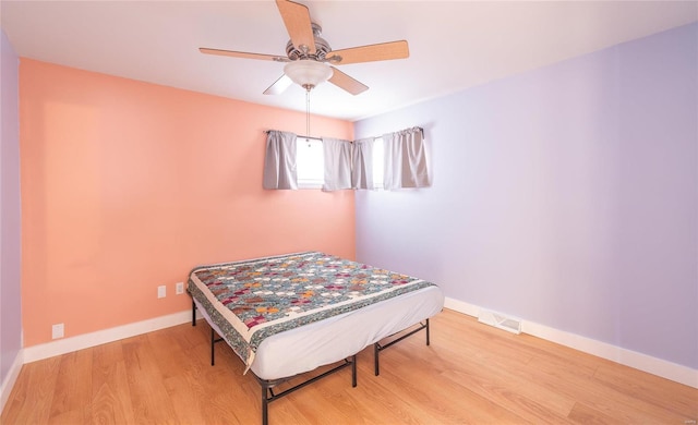 bedroom with a ceiling fan, wood finished floors, visible vents, and baseboards