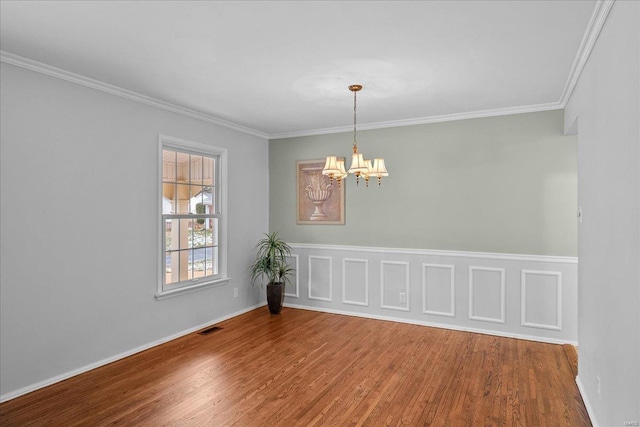 spare room featuring ornamental molding, visible vents, a notable chandelier, and wood finished floors