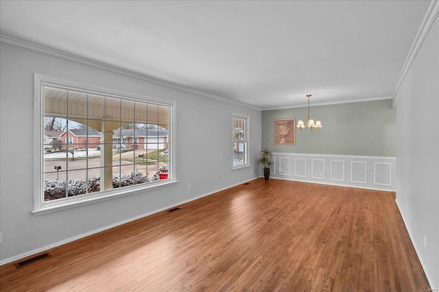 empty room with a healthy amount of sunlight, wood finished floors, visible vents, and a notable chandelier