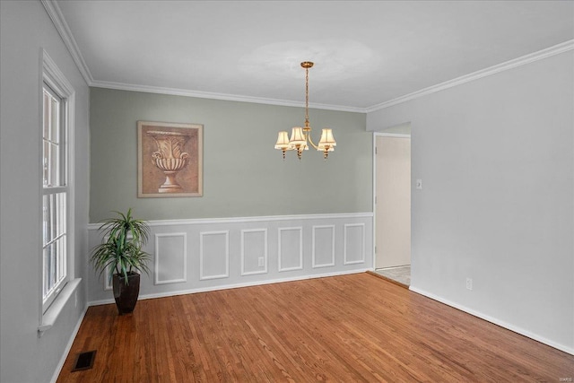 spare room featuring ornamental molding, visible vents, a notable chandelier, and wood finished floors