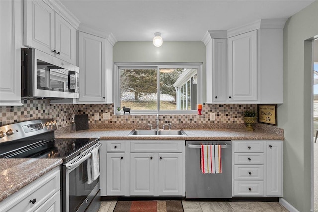 kitchen featuring stainless steel appliances, decorative backsplash, white cabinetry, a sink, and baseboards