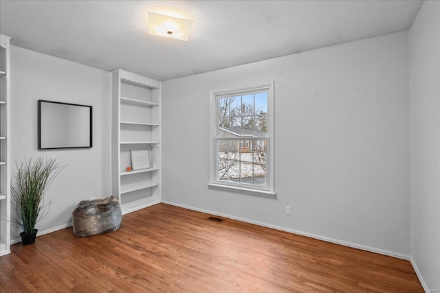 unfurnished room featuring built in shelves, visible vents, baseboards, and wood finished floors