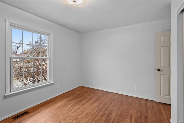 spare room featuring baseboards, visible vents, a wealth of natural light, and wood finished floors