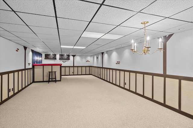 below grade area with a paneled ceiling, carpet flooring, and a notable chandelier