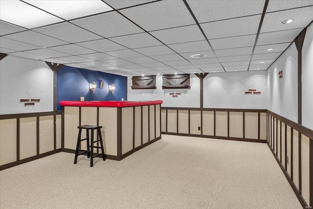 basement with a wainscoted wall, a drop ceiling, and carpet