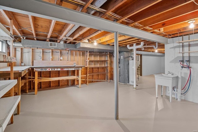 unfinished below grade area featuring water heater, a workshop area, a sink, and visible vents