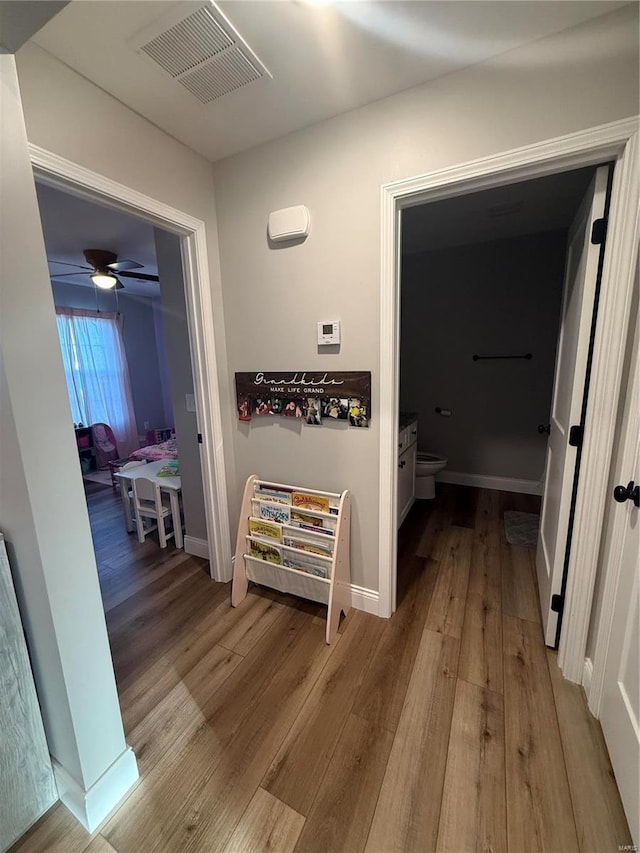 hallway with wood finished floors, visible vents, and baseboards