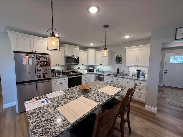 kitchen with a breakfast bar, appliances with stainless steel finishes, white cabinetry, and dark wood-type flooring