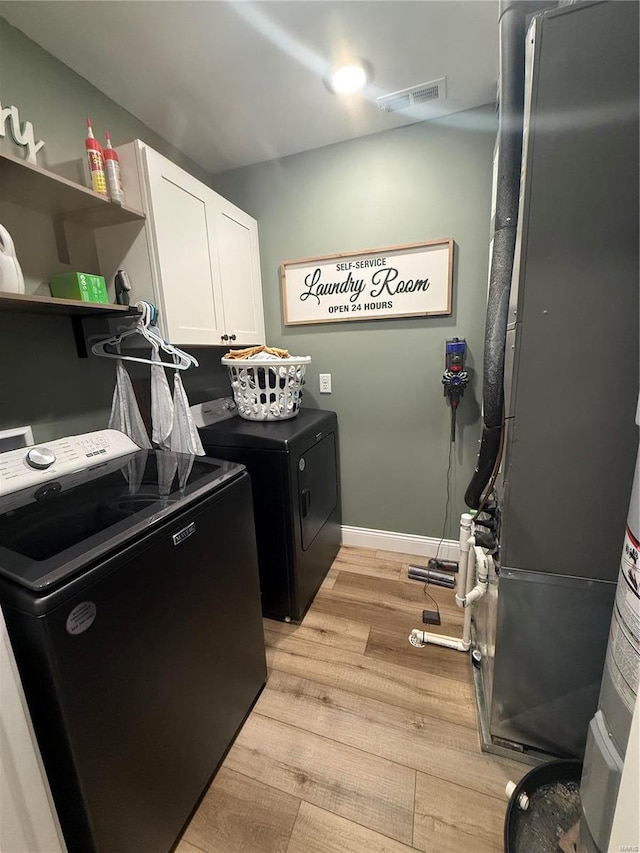 laundry room with visible vents, light wood-style flooring, washer and clothes dryer, cabinet space, and baseboards