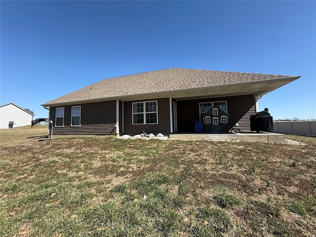 rear view of house with a lawn and roof with shingles