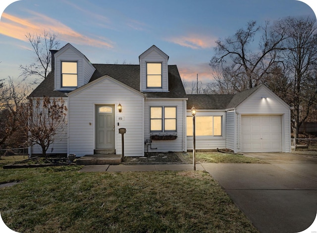 cape cod-style house featuring a yard, driveway, a shingled roof, and an attached garage