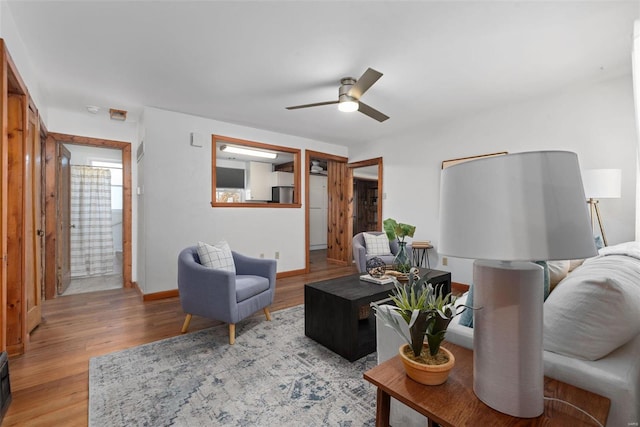 living area featuring light wood finished floors, a ceiling fan, and baseboards