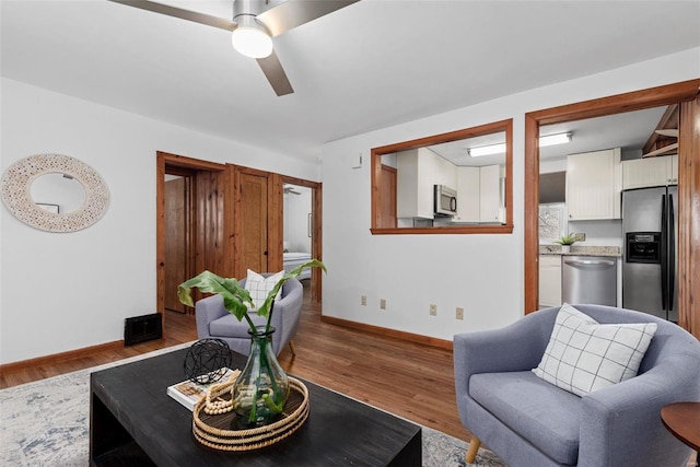 living area featuring a ceiling fan, baseboards, and wood finished floors