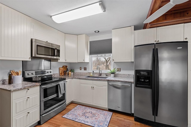 kitchen with stainless steel appliances, a sink, light wood-style flooring, and white cabinetry