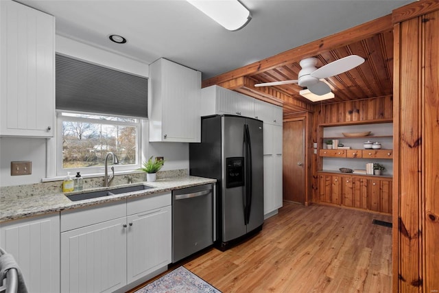 kitchen featuring light stone counters, appliances with stainless steel finishes, white cabinetry, a sink, and light wood-type flooring