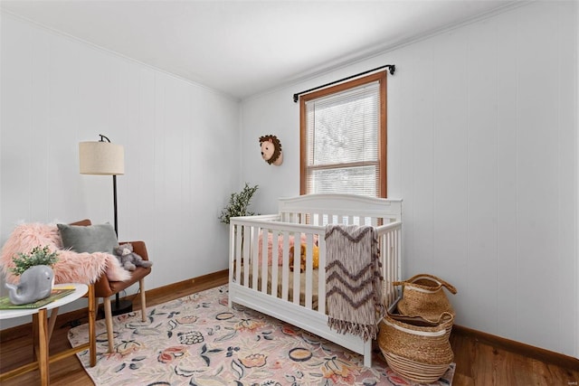 bedroom with light wood-type flooring, baseboards, and a crib