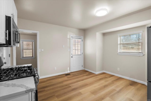 kitchen featuring baseboards, light stone counters, stainless steel appliances, light wood-type flooring, and white cabinetry