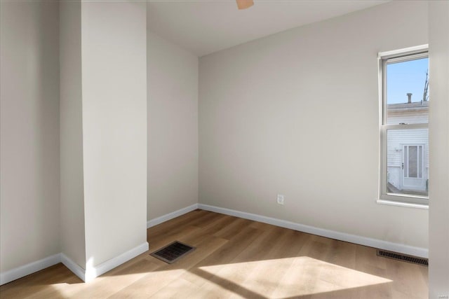 empty room with wood finished floors, visible vents, and baseboards