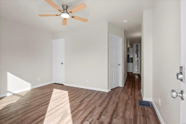 spare room with a ceiling fan, visible vents, baseboards, and wood finished floors