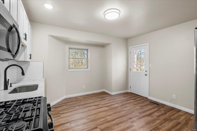 kitchen with baseboards, stainless steel microwave, light wood-style floors, white cabinetry, and a sink