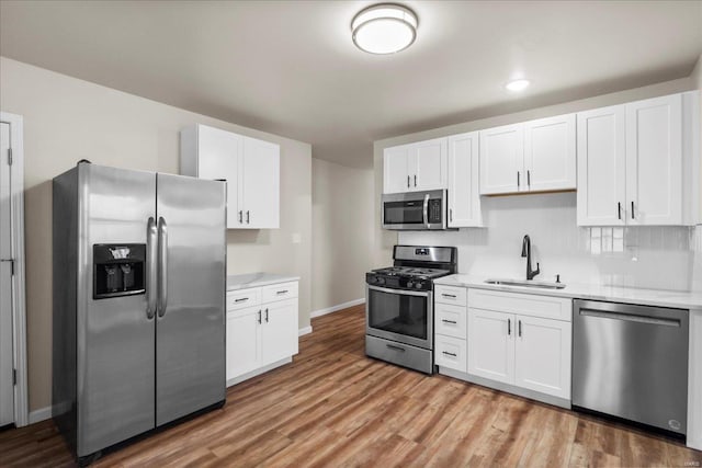 kitchen with light wood-type flooring, appliances with stainless steel finishes, white cabinets, and a sink