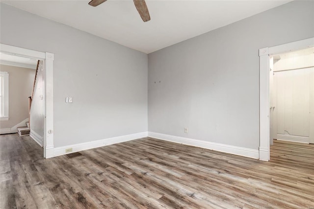 empty room with stairway, wood finished floors, a ceiling fan, and baseboards