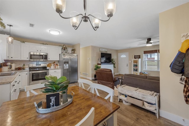 dining room featuring light wood-type flooring, baseboards, visible vents, and ceiling fan with notable chandelier