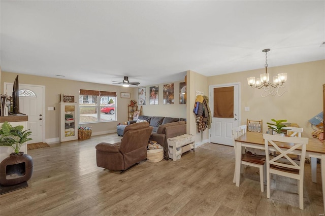 living room featuring light wood finished floors, baseboards, and ceiling fan with notable chandelier