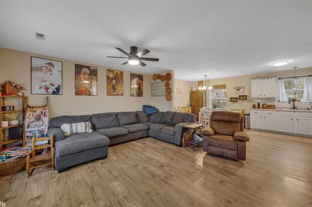 living room featuring light wood-type flooring, visible vents, and ceiling fan with notable chandelier